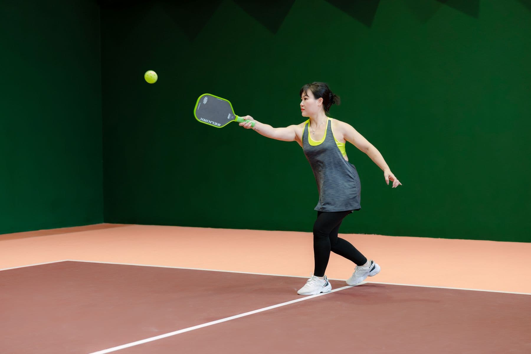 A player mid-forehand on an indoor pickleball court.