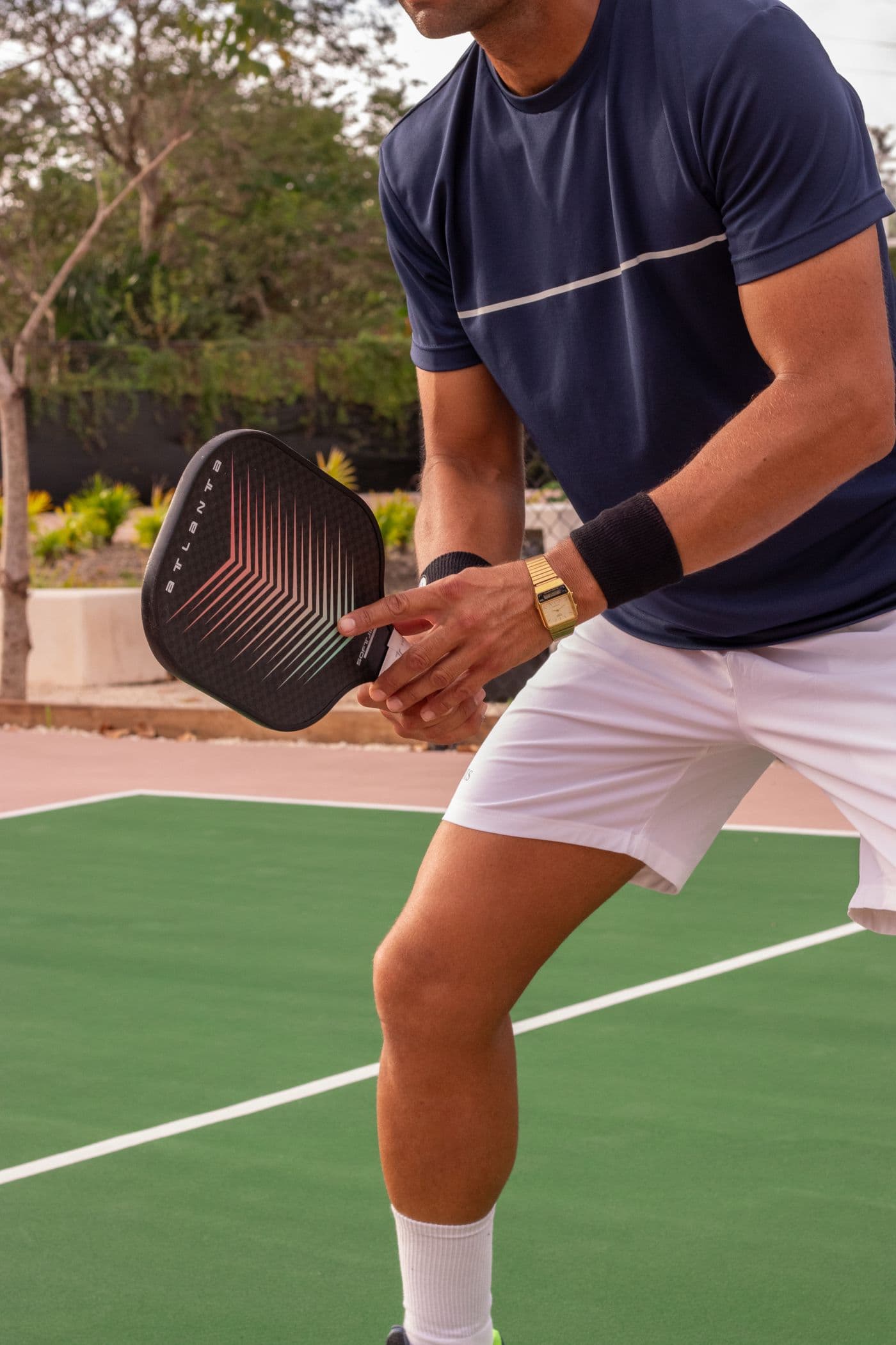A player crouched at the baseline holding a paddle and ball, about to serve. Face out of frame.